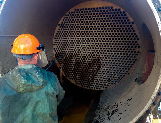 Technician cleaning a heat exchanger with a high-pressure hydraulic unit.